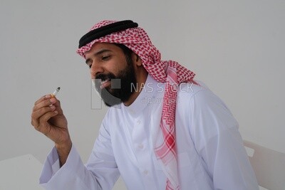 Saudi man wearing a white thobe and shemagh takes a deep breath from a cigarette, tobacco addiction, cigarette addiction, harmful and toxic substance abuse, harmful behavioral habits, no smoking, Saud