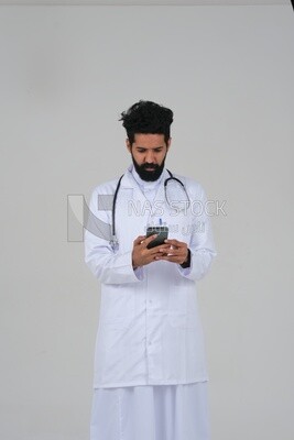 Saudi man wearing a medical coat and a stethoscope, using his mobile, white background, medicine and health care, Saudi model
