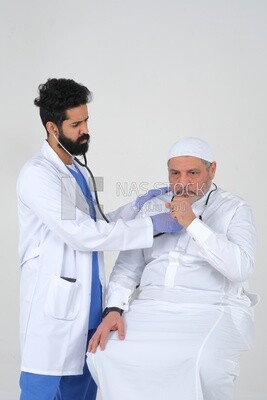 رجل سعودي يرتدي معطفًا طبيًا وسماعة طبيب ، يستمع الطبيب إلى نبضات قلب المريض ، والخلفية البيضاء ، والطب والرعاية الصحية ، موديل سعودى