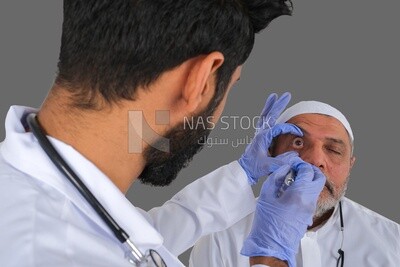 رجل سعودي يرتدي معطفا طبيا وسماعة طبية ، يفحص عيون المريض ، خلفية بيضاء ، الطب والرعاية الصحية ، موديل سعودى
