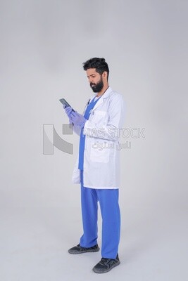 رجل سعودي يرتدي معطفًا طبيًا وسماعة طبيب يتسخدم هاتفه المحمول ، الخلفية البيضاء ، الطب والرعاية الصحية