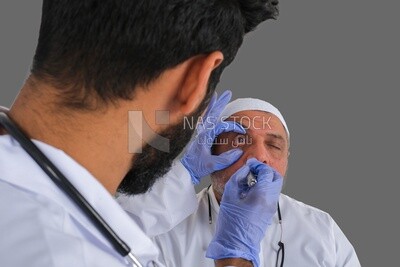 Saudi man wearing a medical coat and a stethoscope, checking the patient&#39;s eyes, white background, medicine and health care, Saudi model