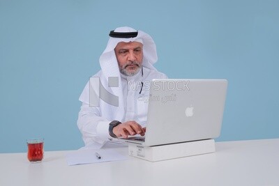 Saudi man sitting and working on a laptop, a cup of tea, business feasibility study, Saudi model