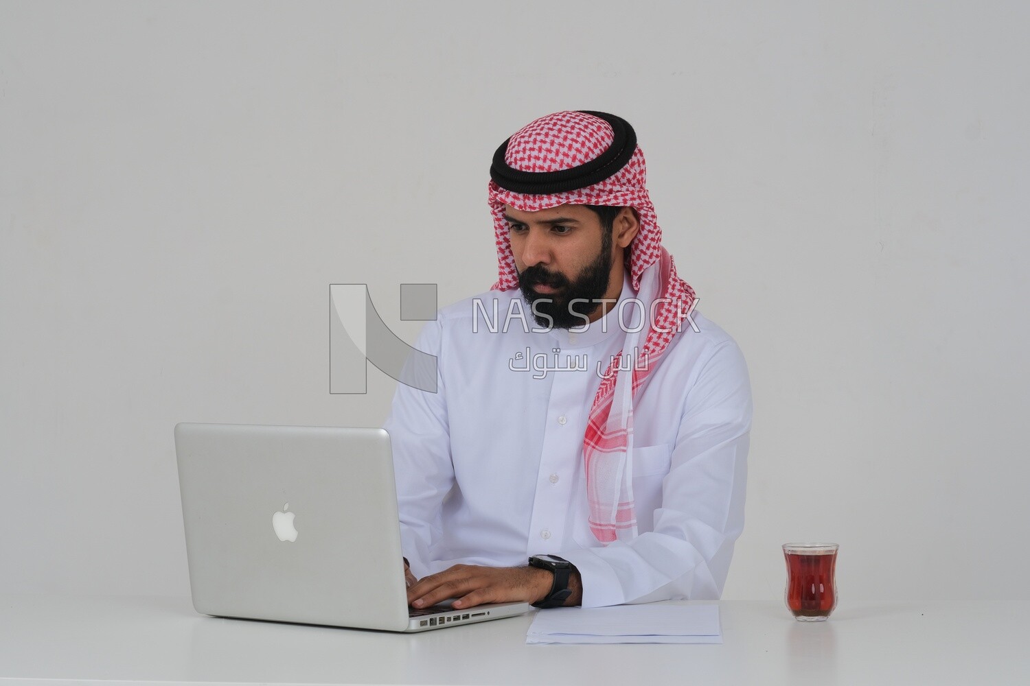 Saudi man sitting and working on a laptop, a cup of tea, business feasibility study, white background, Saudi model