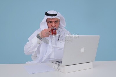 رجل سعودي يجلس ويعمل على جهاز كمبيوتر محمول ، يحتسى فنجان شاي ، دراسة جدوى أعمال ، موديل سعودي