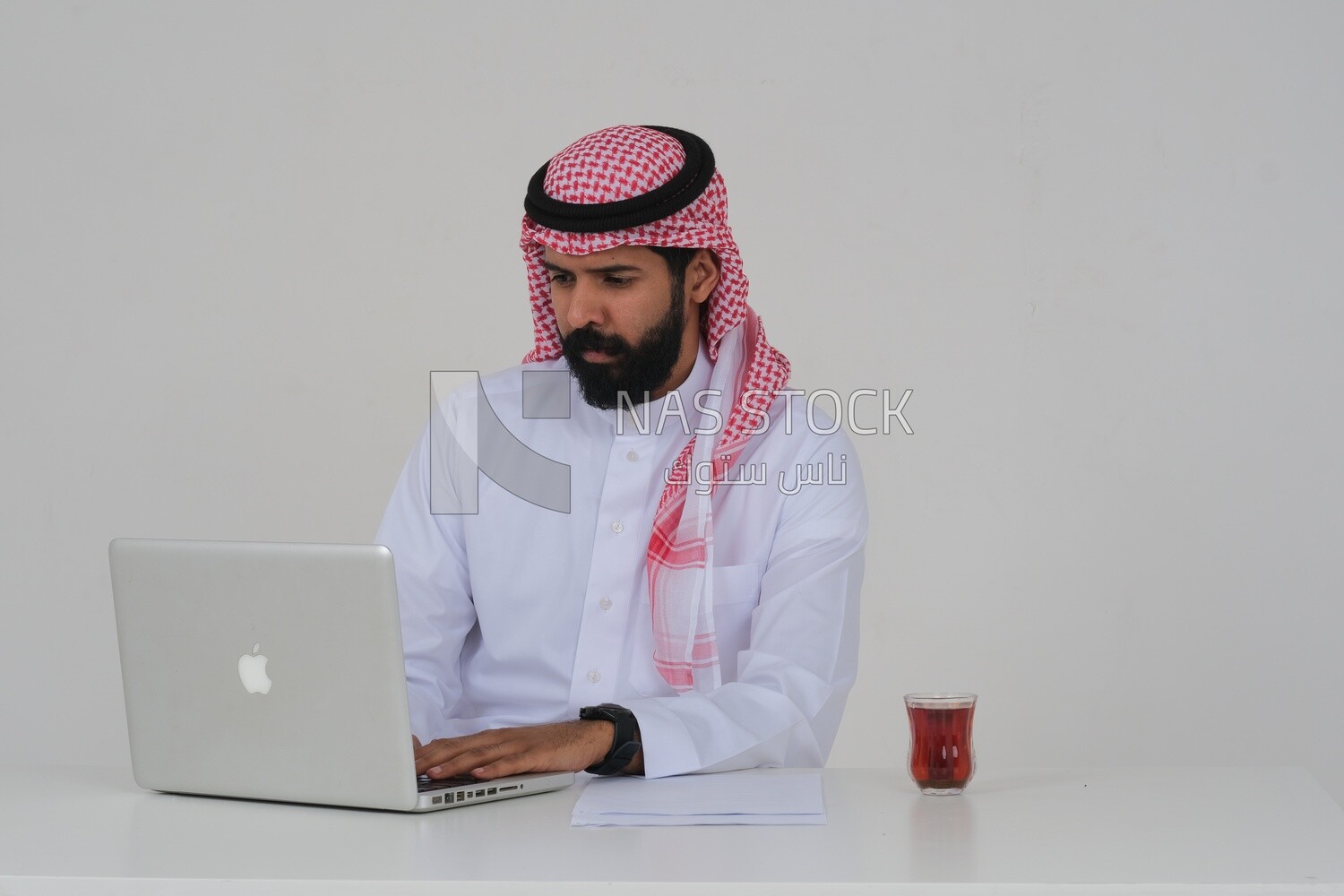 Saudi man sitting and working on a laptop, a cup of tea, business feasibility study, white background, Saudi model