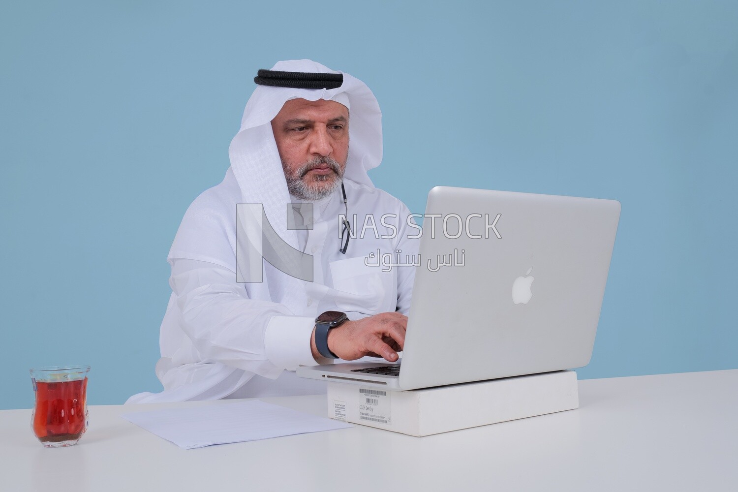 Saudi man sitting and working on a laptop, a cup of tea, business feasibility study, Saudi model