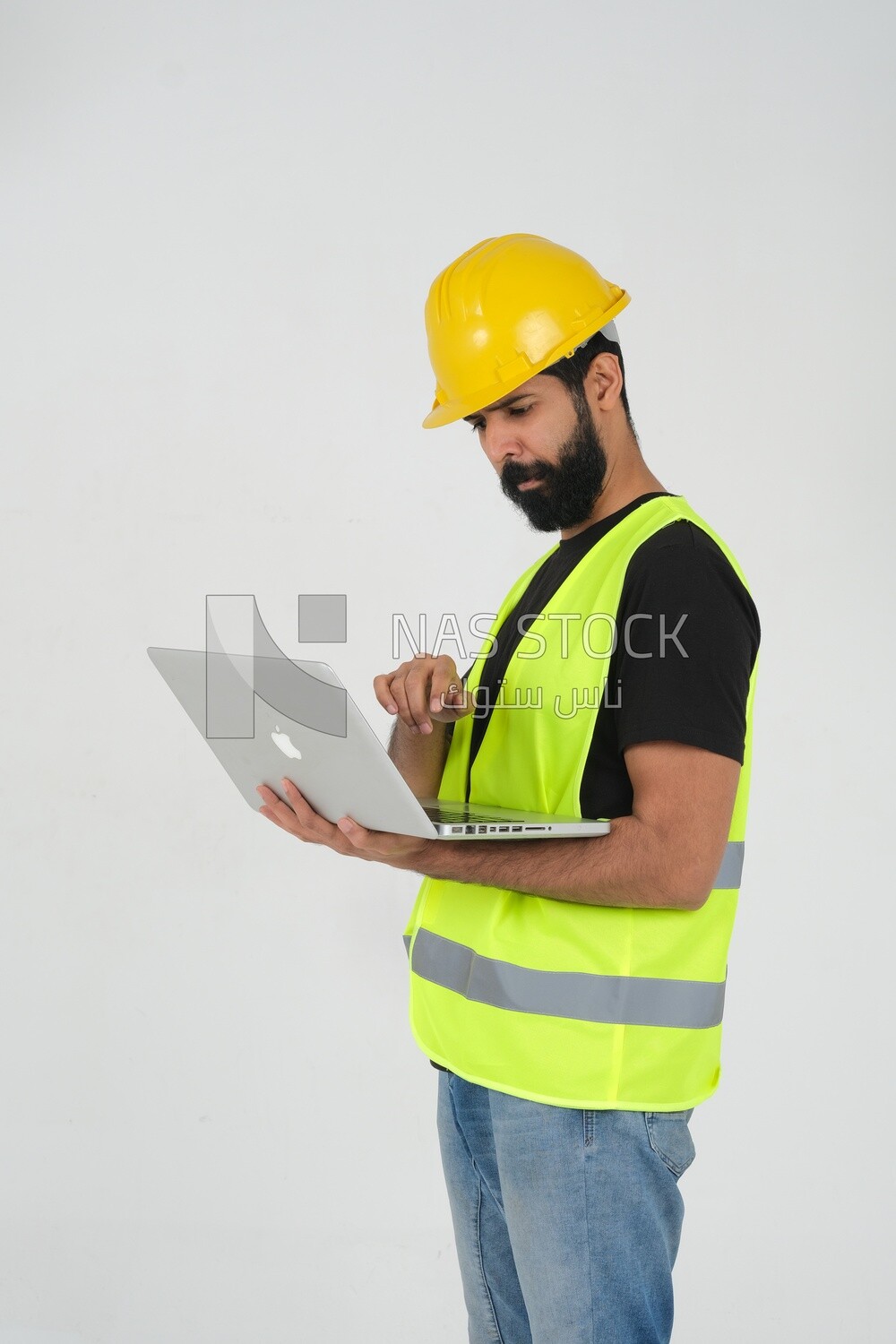 Saudi engineer wearing a work helmet and protective jacket, holding a laptop and looking away, engineering professions and jobs, white background, Saudi model