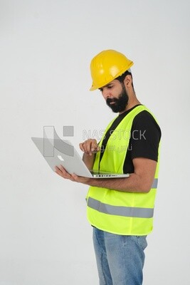 Saudi engineer wearing a work helmet and protective jacket, holding a laptop and looking away, engineering professions and jobs, white background, Saudi model