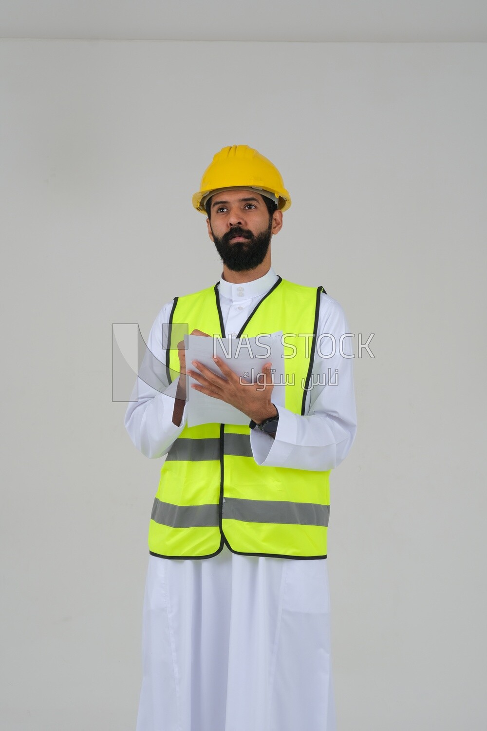 Saudi engineer wearing a work helmet and protective jacket, writing and taking notes, engineering professions and jobs, white background, Saudi model