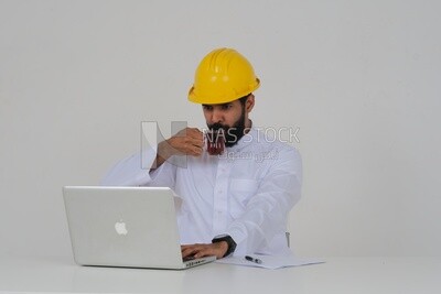 Saudi engineer wearing a work hat sitting and working on the laptop, drinking a cup of tea, engineering professions and jobs, white background, Saudi model