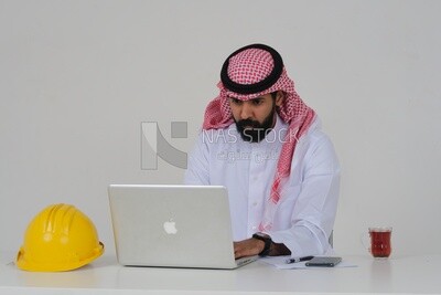 مهندس سعودي ، جالسًا ويعمل على اللاب توب ، كوب شاي ، قبعة عمل ، مهن هندسية ووظائف ، خلفية بيضاء ، موديل سعودي