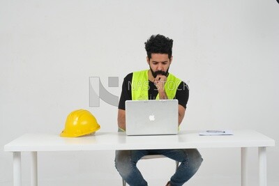Saudi engineer wearing a safety vest sitting and working on the laptop, engineering professions and jobs, white background, Saudi model