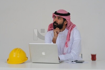 Saudi engineer wearing a work hat sitting in front of the laptop, writing notes , engineering professions and jobs, white background, Saudi model