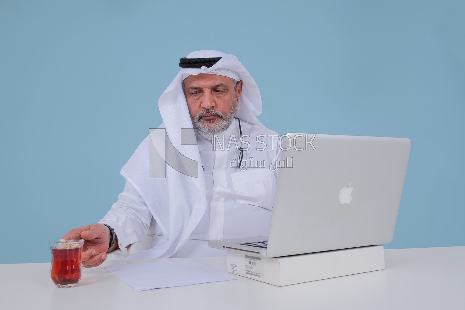 Saudi man sitting and working on a laptop, a cup of tea, business feasibility study, Saudi model