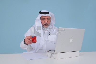 Saudi man sitting and working on a laptop, drinking a cup of tea, business feasibility study, Saudi model
