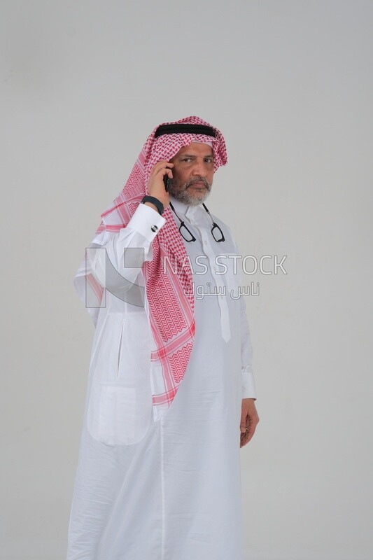 Saudi man in traditional Saudi dress, holding a mobile phone and making a phone call, Saudi model, white background