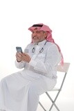 رجل سعودي يرتدي ثوباً أبيض يجلس على كرسي ، يحمل هاتفه المحمول ، ثقة بالنفس ، خلفية بيضاء ، موديل سعودى