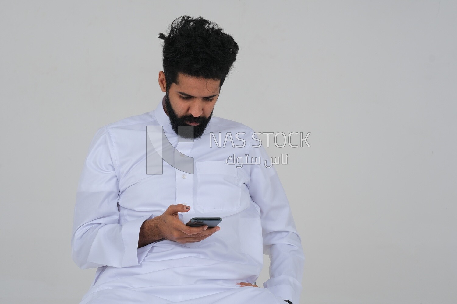 Saudi man in traditional Saudi dress, holding a mobile phone and checking it, Saudi model, white background