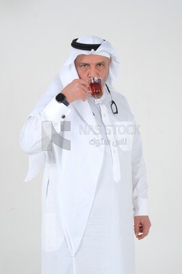 Saudi man wearing a white dress sitting on a chair, carrying a cup of tea and looking at it, self-confidence, white background, Saudi model