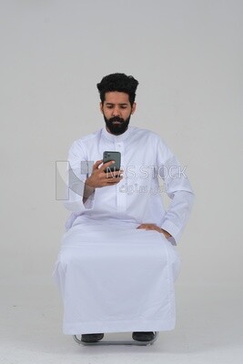 Saudi man wearing a white dress sitting on a chair, carrying his mobile phone, self-confidence, white background, Saudi model