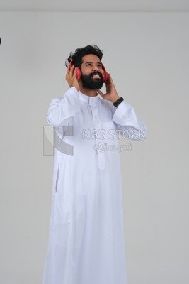 Saudi man puts on a headset and enjoys listening to songs and music, recording songs and audios, voiceover, presenting radio programs, talent and art, white background, Saudi model