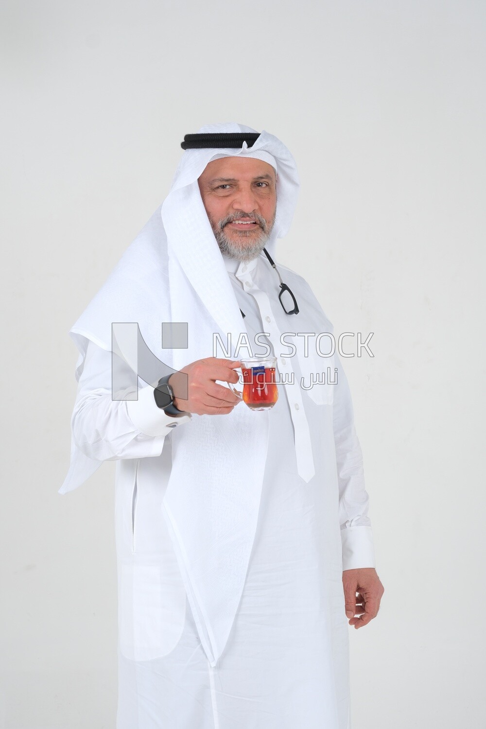 old Saudi man wearing a white dress sitting on a chair, carrying a cup of tea, self-confidence, white background, Saudi model