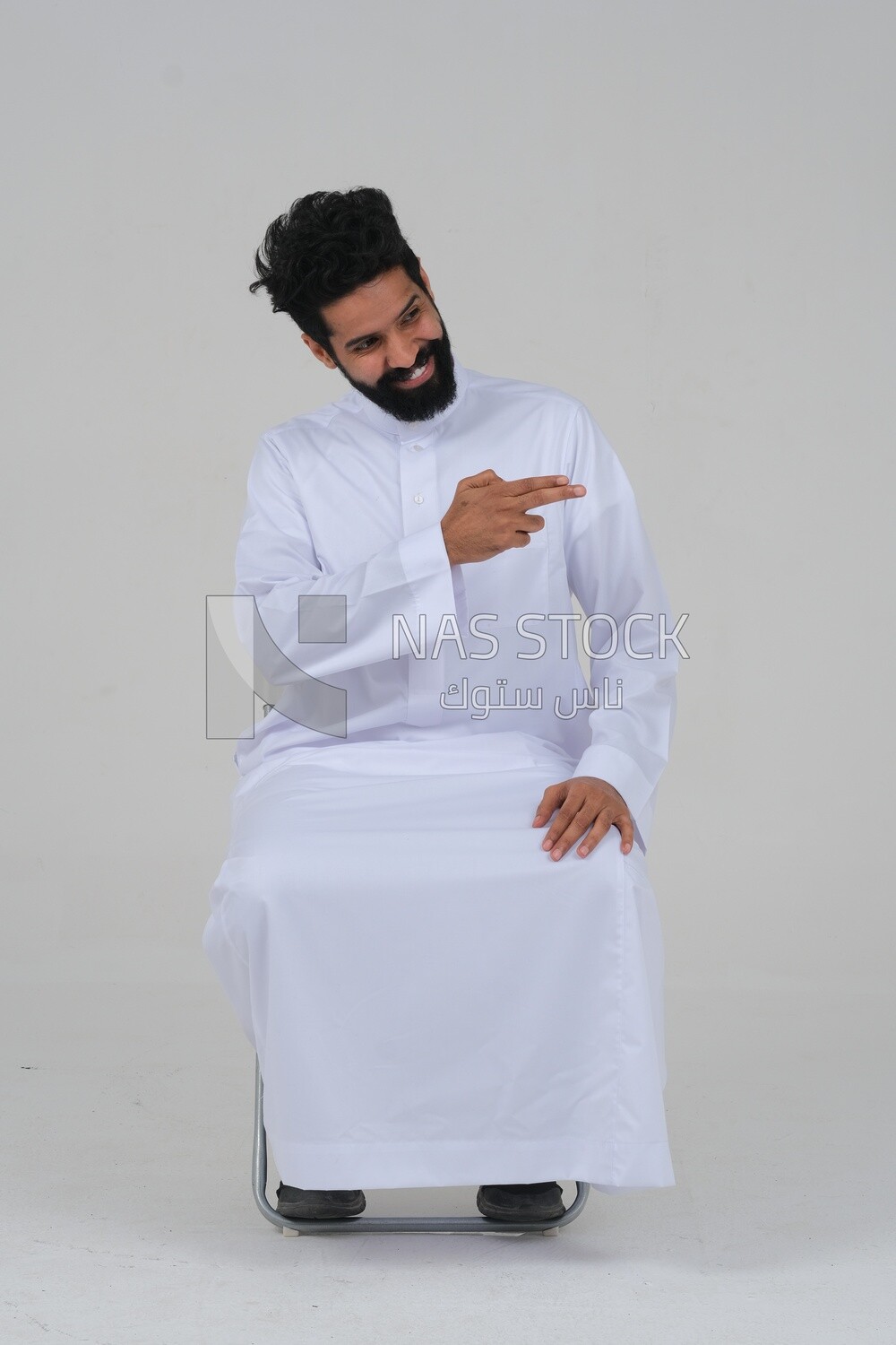 saudi man wearing the Saudi thobe sitting on a chair, hand gestures pointing to the right, movements indicating this place, this website, white background