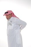 Saudi man with his hand on his back, feeling a state of pain, close-up, a young Saudi man wearing a white dress with a shemagh and headband, white background, a side view of an elderly man feeling t