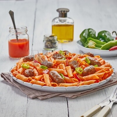 Side view of a dining table containing pasta with sausage and appetizers