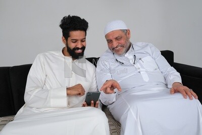 Saudi man spending time with his father sitting on the sofa, pointing at the phone, white background, Saudi model