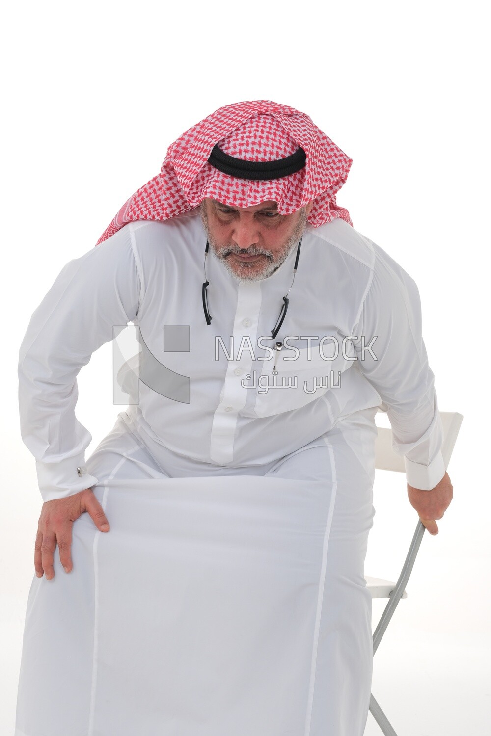 elderly Saudi man trying to sit on a chair, back and spine pain, fatigue and exhaustion, muscle spasms, health problems, white background, Saudi model