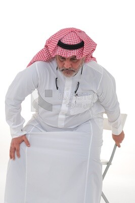 elderly Saudi man trying to sit on a chair, back and spine pain, fatigue and exhaustion, muscle spasms, health problems, white background, Saudi model