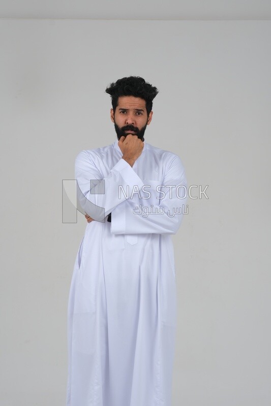 Saudi man wearing a traditional Saudi dress, putting his hand on his face with gestures and facial expressions and hands indicating boredom, reflecting on a problem solution, thinking about a topic, f