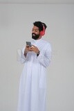 Saudi man puts on a headset and enjoys listening to songs and music, recording songs and audios, voiceover, presenting radio programs, talent and art, white background, Saudi model