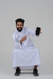 Saudi man using a mobile phone pointing on it, communicating with individuals, online requests and marketing, social relations, using technical devices, white background