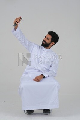 Saudi man using a mobile phone, taking a selfie, communicating with individuals, online requests and marketing, social relations, using technical devices, white background