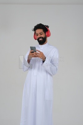 Saudi man puts on a headset and enjoys listening to songs and music, recording songs and audios, voiceover, presenting radio programs, talent and art, white background, Saudi model