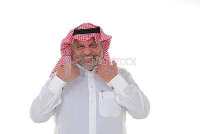 old Saudi man pointing his hand over his teeth,  a young Saudi man wearing a white dress with a shemagh and headband, white background, an elderly man pointing his index finger at his teeth