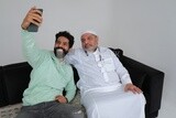 Saudi man spending time with his father sitting on the sofa, taking a selfie, white background, Saudi model