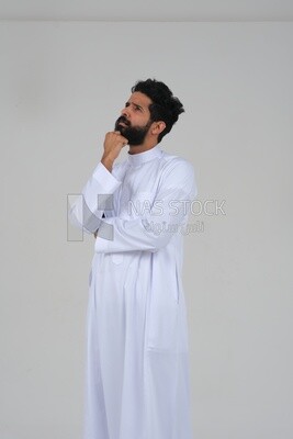 saudi man wearing a traditional Saudi dress, putting his hand on his face with gestures and facial expressions and hands indicating boredom, reflecting on a problem solution, thinking about a topic, f