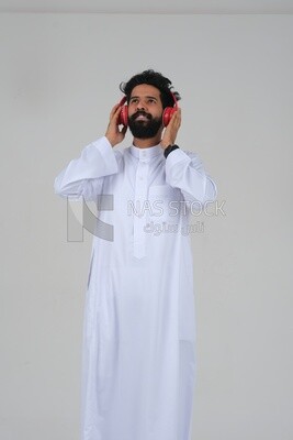 Saudi man puts on a headset and enjoys listening to songs and music, recording songs and audios, voiceover, presenting radio programs, talent and art, white background, Saudi model
