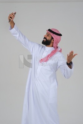 Saudi man using a mobile phone, taking a selfie, communicating with individuals, online requests and marketing, social relations, using technical devices, white background