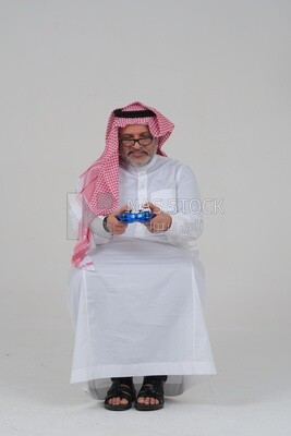 elderly saudi man holding a joystick in his hand and playing video games, with gestures and expressions that indicate focus and harmony, fun and entertainment with video games, PlayStation