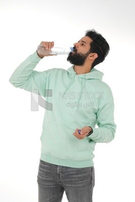 Saudi man wearing casual clothes, drinking from a water bottle, Saudi model, white background