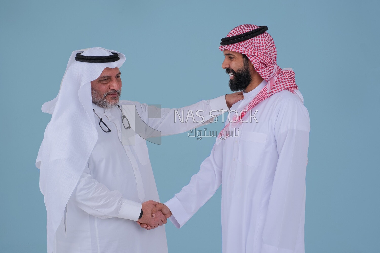 Two Saudi  businessmen shaking hands in traditional Saudi dress gesturing with handshake gesture, welcome, agreement, peace, acquaintance, dating concept