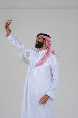 Saudi man using a mobile phone, taking a selfie, communicating with individuals, online requests and marketing, social relations, using technical devices, white background