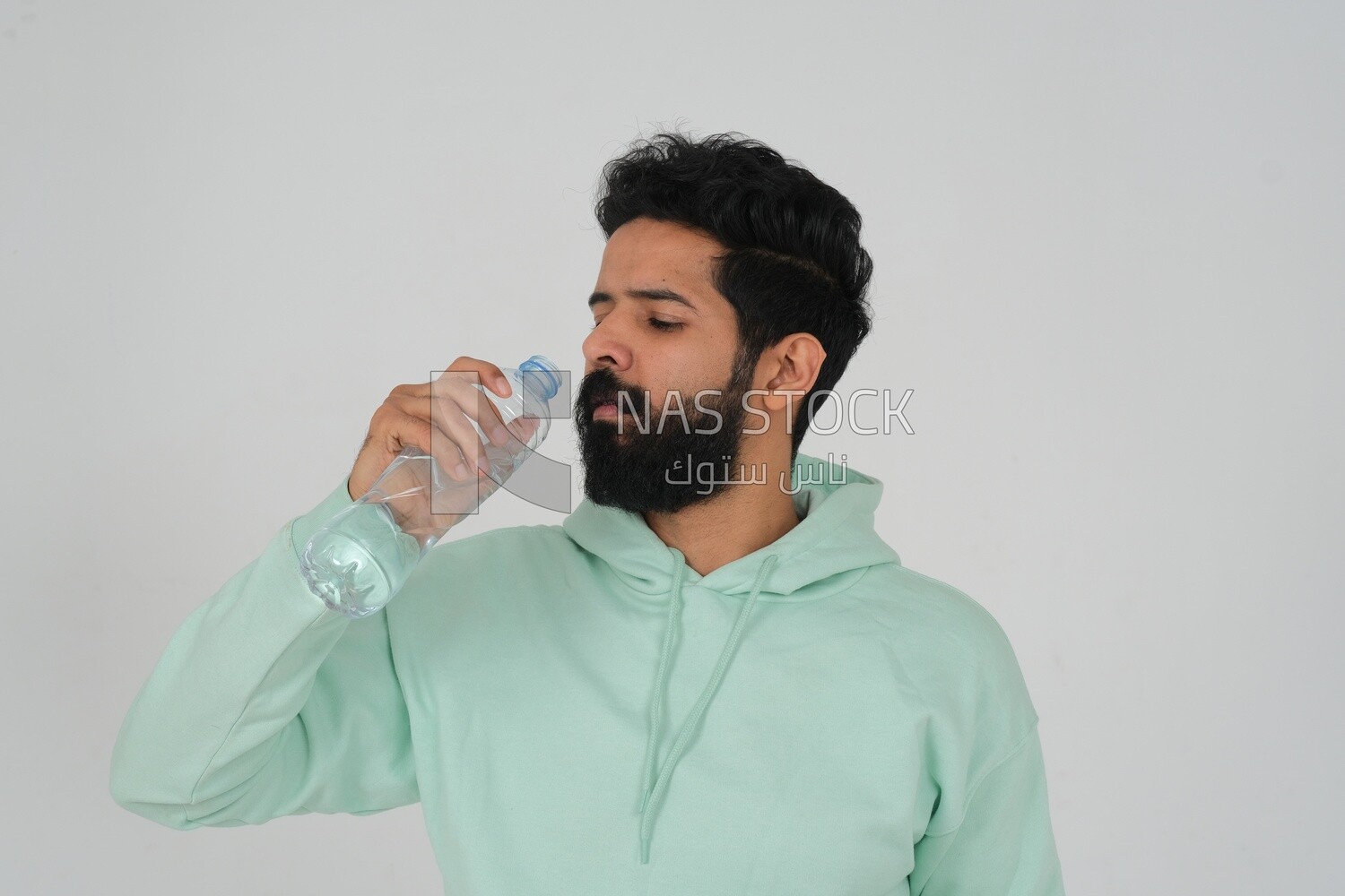 Saudi man wearing casual clothes, drinking from a water bottle, Saudi model, white background