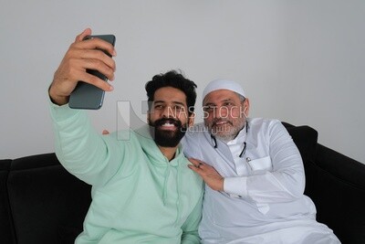 Saudi man spending time with his father sitting on the sofa, taking a selfie, white background, Saudi model