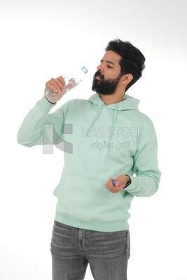 Saudi man wearing casual clothes, drinking from a water bottle, Saudi model, white background